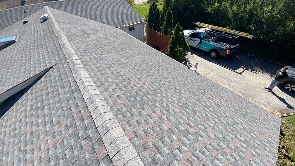 Close-up of roof ridge and asphalt shingles with work truck below