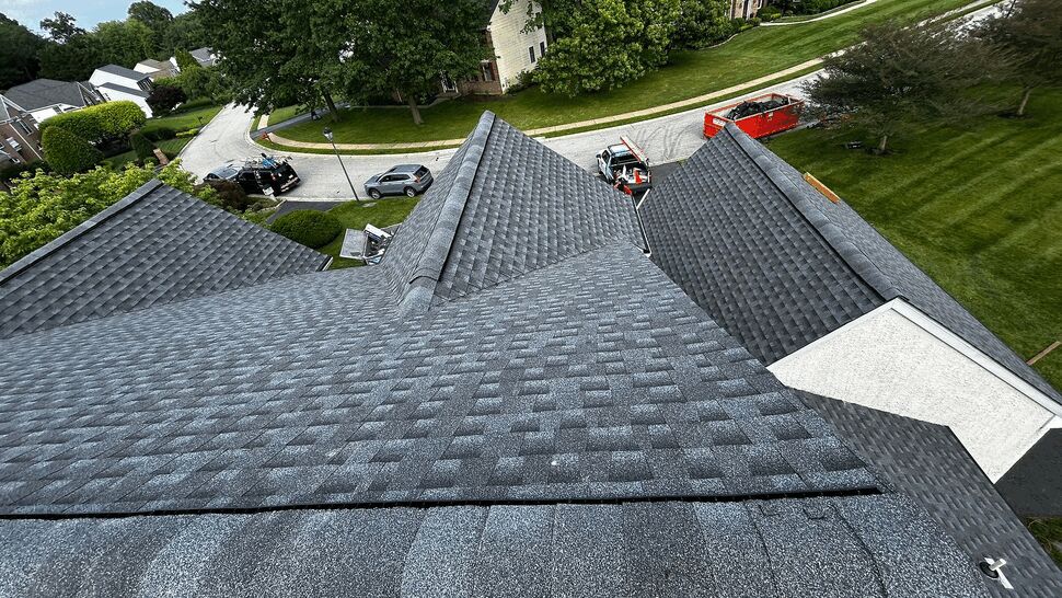 High-angle view down a multi-plane roof showing ridge lines and crew vehicles