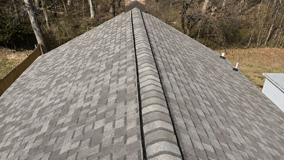 Close view of a shingled roof ridge with chimney in background