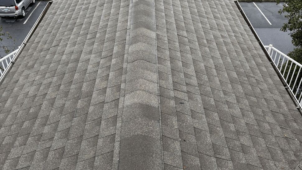 Gray shingle roof ridge viewed from above near a parking lot