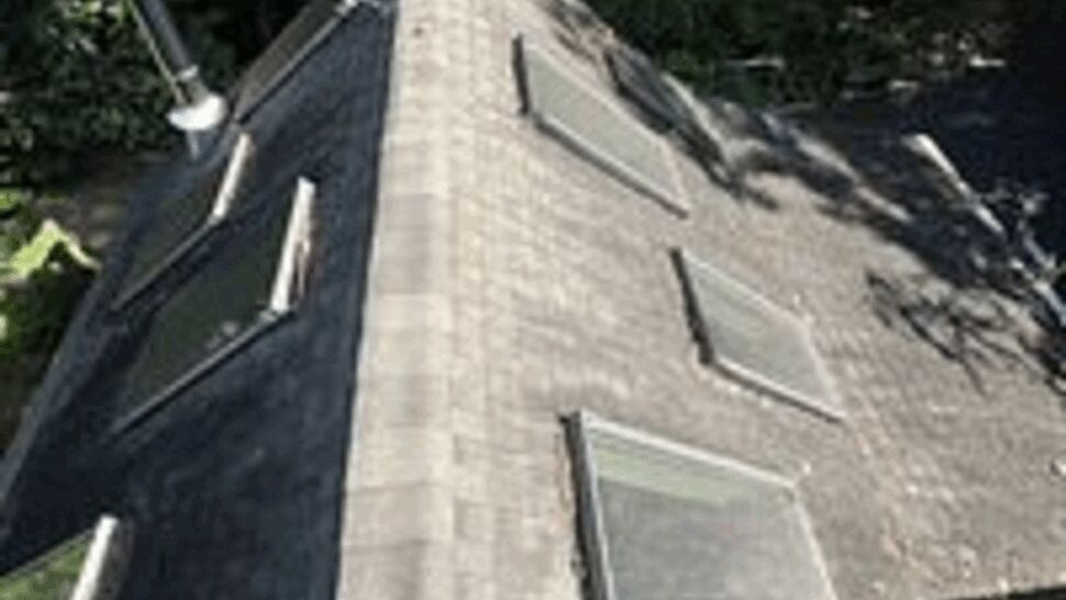 Aerial view down a shingled roof ridge with multiple skylights and a worker boot.
