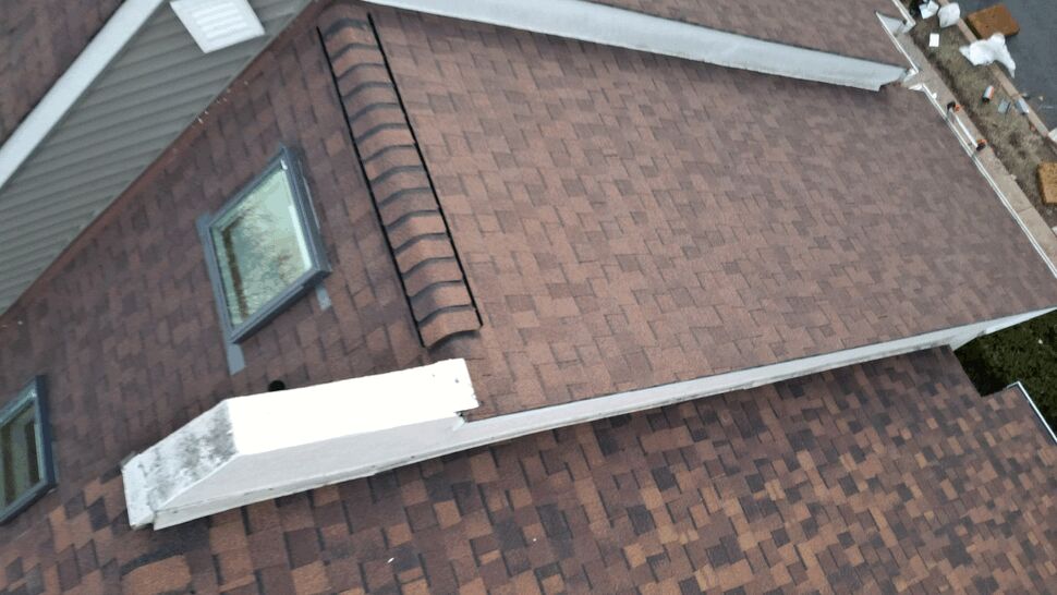 Tilted close aerial view of roof ridges, skylights, and brown asphalt shingles