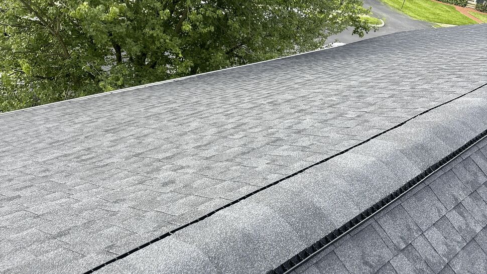Gray shingle roof with a ridge vent above a tree-lined neighborhood