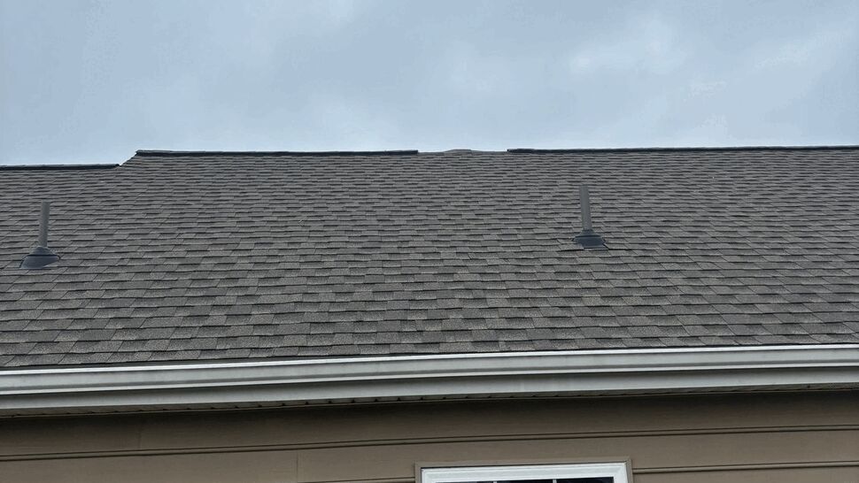 Close-up of asphalt shingle roof ridge with two plumbing vents under a cloudy sky.
