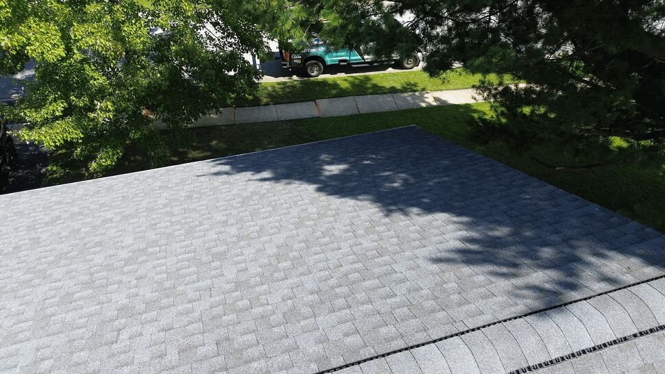 Aerial shingle roof installation | Tycos Roofing And Siding Inc Overhead view of gray asphalt shingle roof with tree shadows and company truck in background.