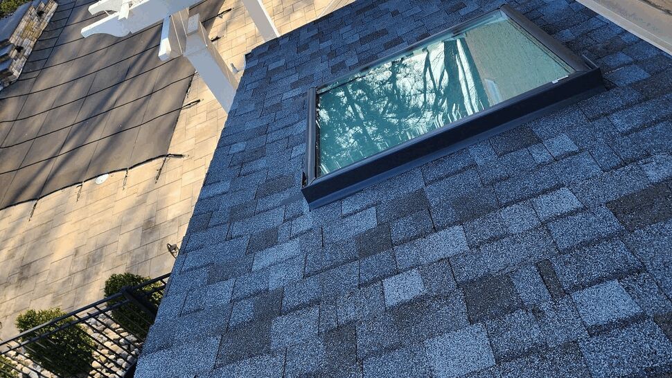 Shingled roof with a skylight next to a white pergola and patio below.