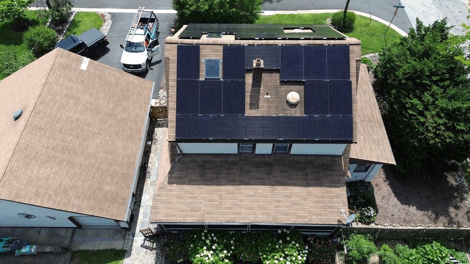 Top-down view of house roof covered with black solar panels and skylights