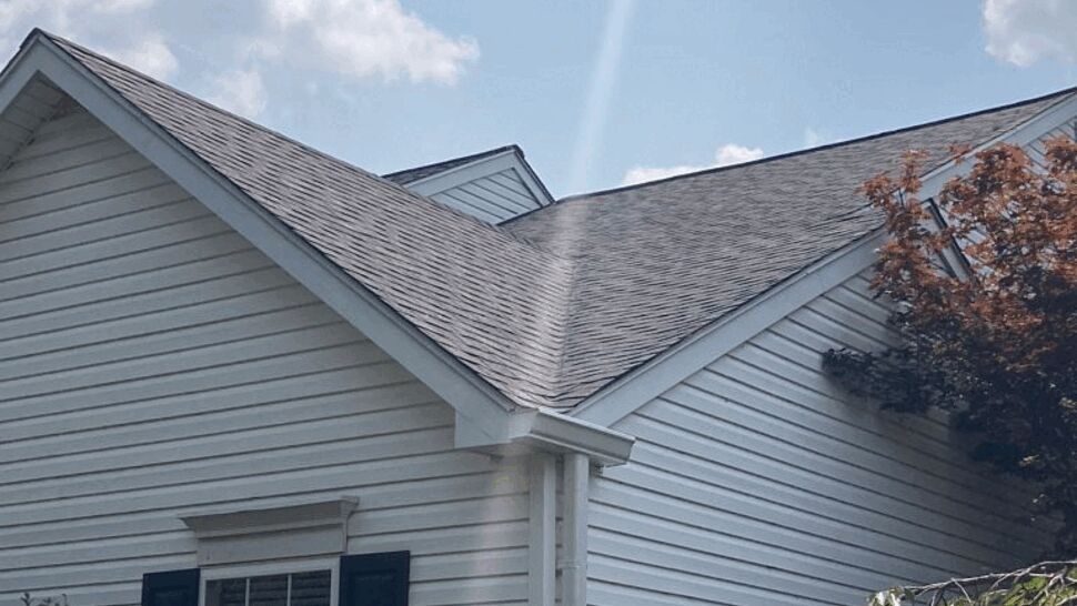 Angle view of a roof valley and ridge above white siding under a blue sky.