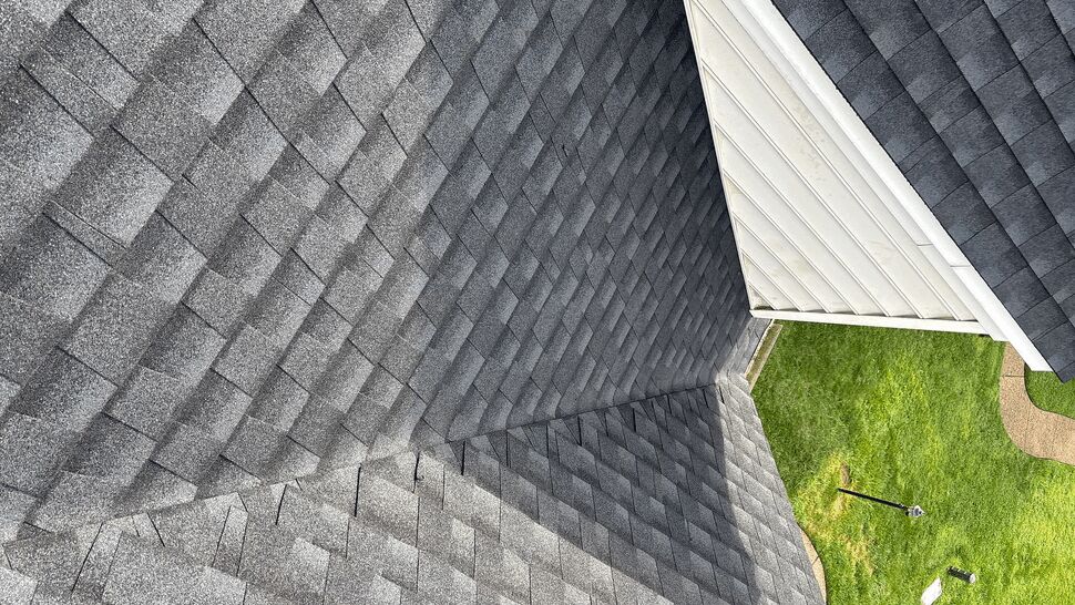 Close-up of a roof valley with shingles and white siding visible