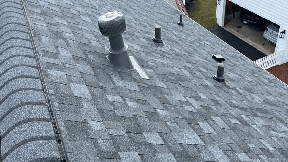 Close-up of gray asphalt shingles with multiple roof vents and ridge vent
