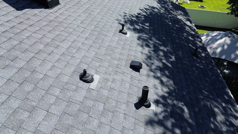 Roof vent flashing detail | Tycos Roofing And Siding Inc Close-up of roof vents and flashing on gray asphalt shingles under sunlight.