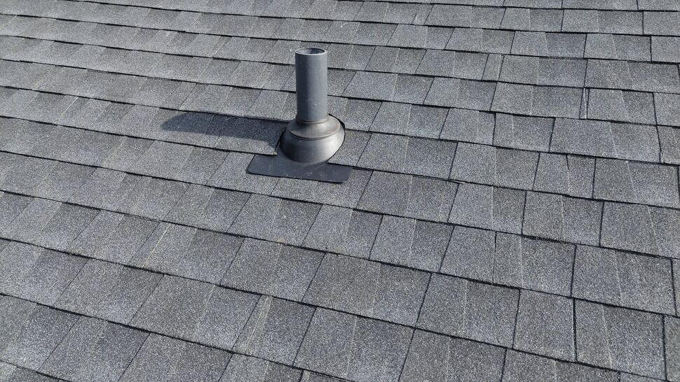 Roof Vent Pipe Boot Detail | Tycos Roofing And Siding Inc Close-up of a plumbing vent pipe boot integrated into gray asphalt shingles.