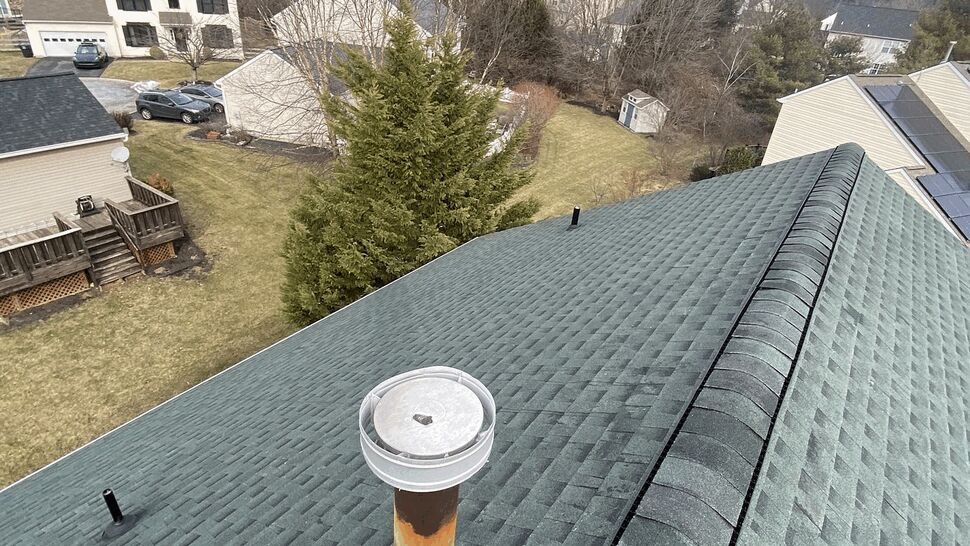 Close-up of green asphalt shingles and a vent pipe on the roof.