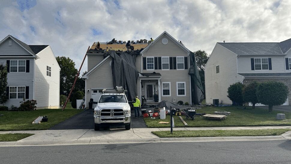 Roof replacement work in progress | Tycos Roofing And Siding Inc Crew on roof removing shingles with tarps and tools while truck sits in driveway