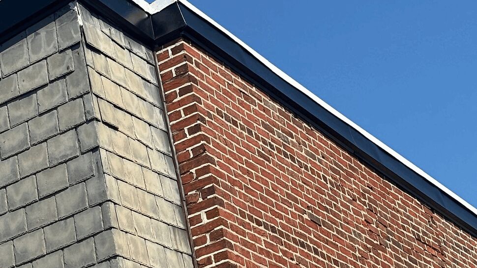 Close-up of a brick and shingle corner with metal roof edge against clear blue sky