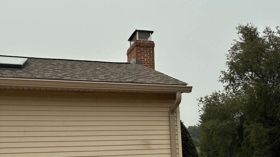 Side view of roofline, chimney and gutter above vinyl siding.