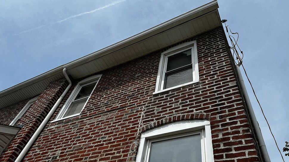 Close-up of brick facade showing roofline, gutters, and second-floor windows.