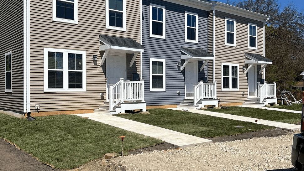 Three newly sided rowhouses with porches and fresh lawn under blue sky.