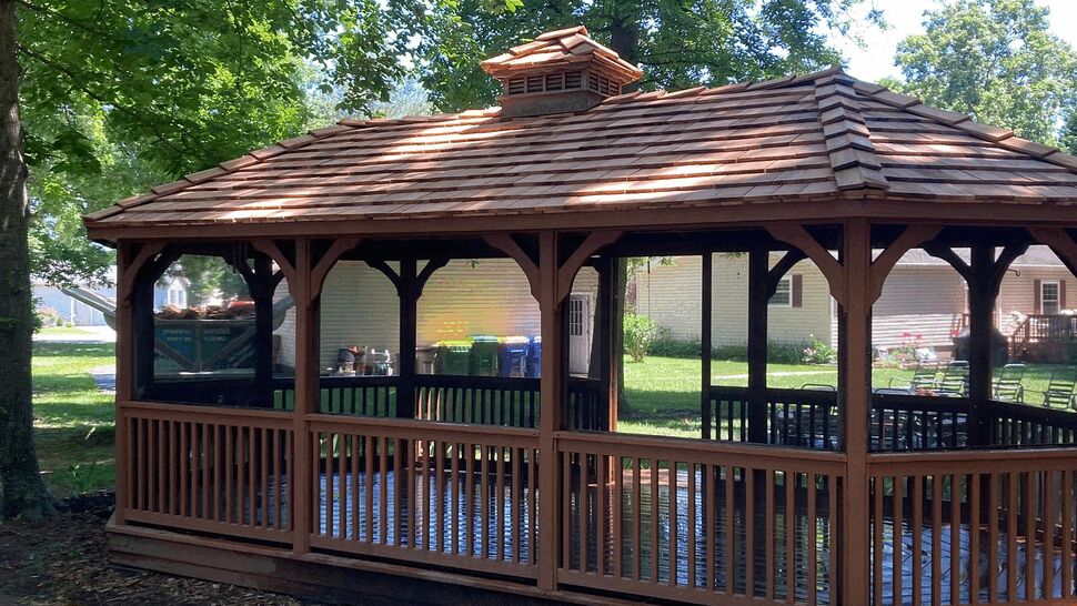 Wide screened gazebo with cedar roof | Tycos Roofing And Siding Inc Wide view of a screened wooden gazebo with cedar-style roof in a shaded backyard.