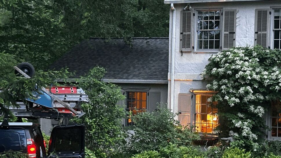 Service van with ladders and equipment parked by house under trees