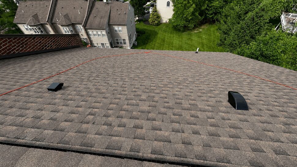 Wide roof expanse with vents and safety rope across asphalt shingles