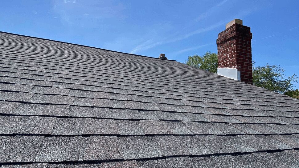 Shingle Roof, Chimney, and Gutters | Tycos Roofing And Siding Inc Gray shingle roof with brick chimney and white gutters under a blue sky.