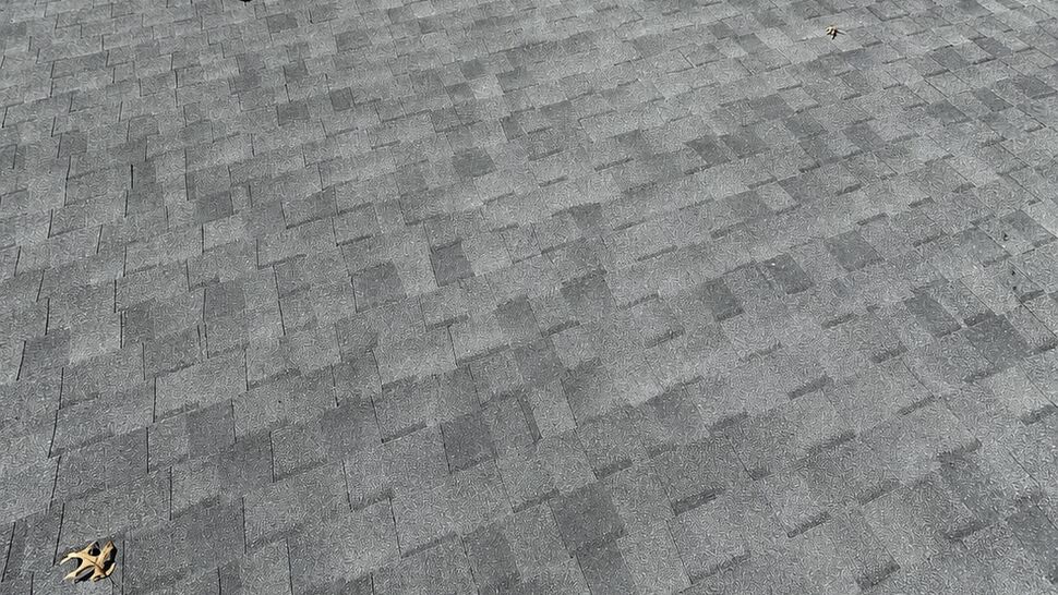 Close-up of gray asphalt shingles and a roof vent with nearby deck visible below.