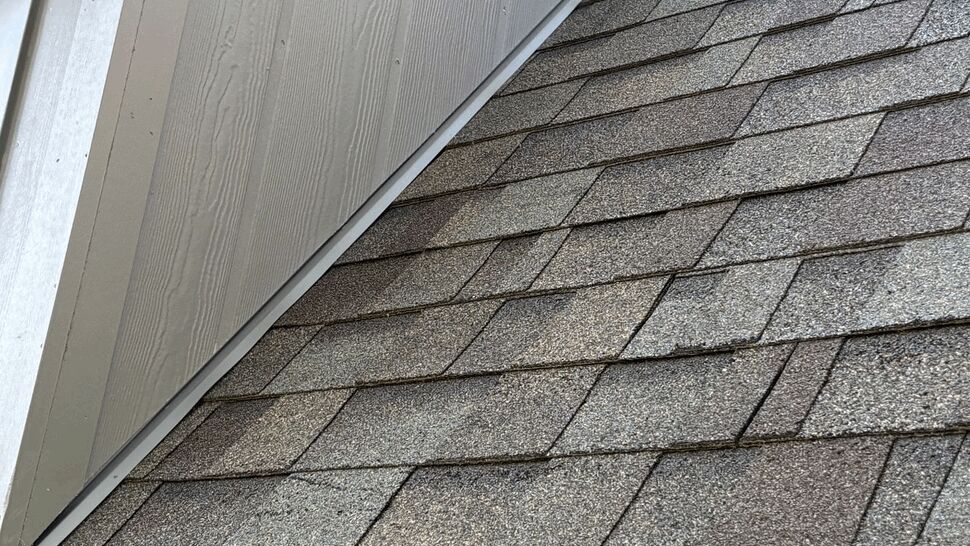 Close-up of asphalt shingles meeting metal flashing along a dormer seam.