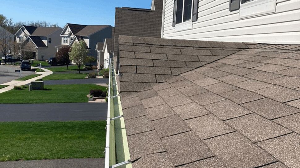 Close-up of asphalt shingles and a white gutter installed along the roof edge