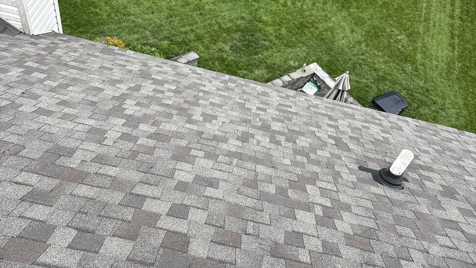 Asphalt shingle roof slope with a white plumbing vent stack and lawn below.