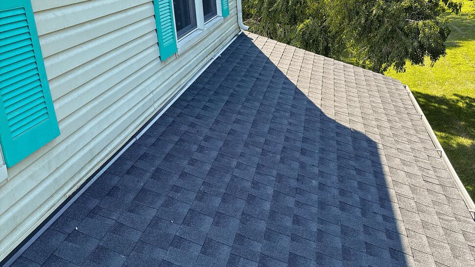 Asphalt shingle roof with white gutter and teal shutters beside a window