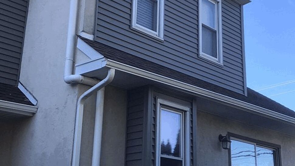 Side view of house with white gutters, downspout and gray siding