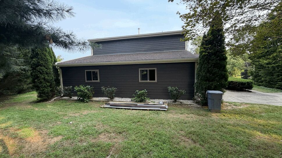 Side Roofline and Exterior Work | Tycos Roofing And Siding Inc Side roofline and dark gray siding with small windows and landscaped yard.