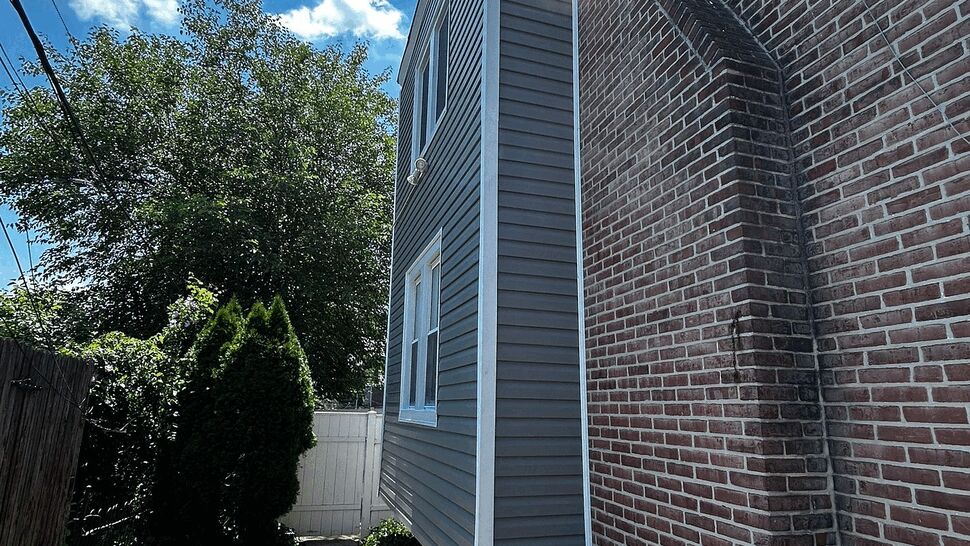 Narrow side yard walkway beside home with new gray siding and brick chimney
