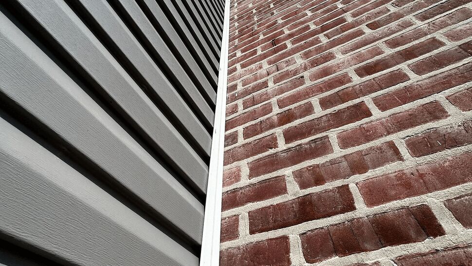 Close-up of gray siding meeting red brick wall with white trim