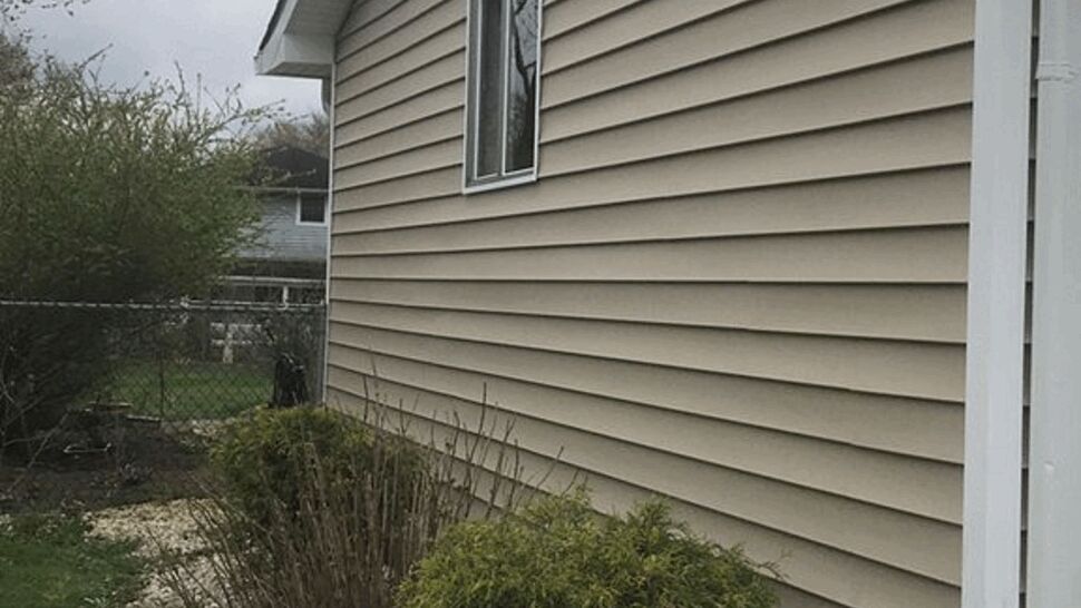 Side elevation with beige vinyl siding, roof overhang and white downspout gutter.