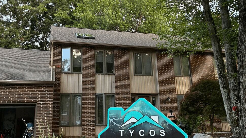 Tycos yard sign centered on lawn with roofline and multiple windows behind