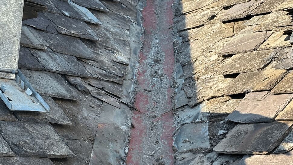 Slate roof valley repair detail | Tycos Roofing And Siding Inc Close-up of slate roof valley with cracked mortar and displaced tiles needing repair