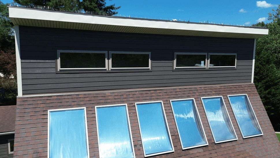 Skylight Installation on Sloped Roof | Tycos Roofing And Siding Inc Shingled sloped roof with six rectangular skylights reflecting blue sky.