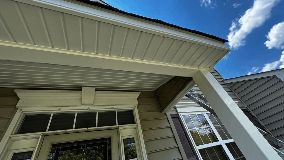 Close view of soffit, fascia and gutter edge along porch roofline against blue sky.