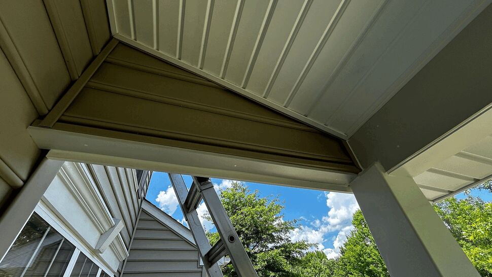 Soffit and trim siding repair | Tycos Roofing And Siding Inc Under-porch view of soffit panels, trim and ladder during exterior work.