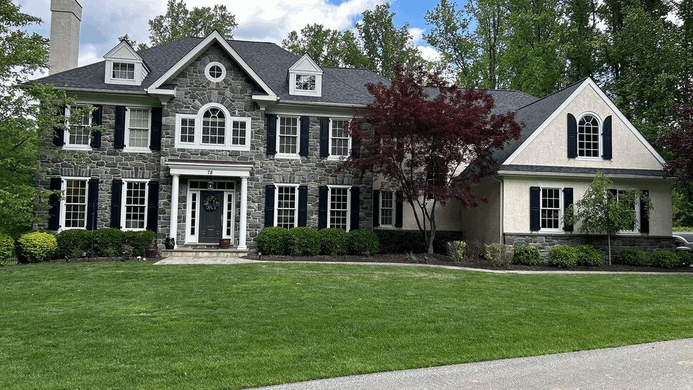 Front view of stone colonial house with dark shingle roof and manicured lawn