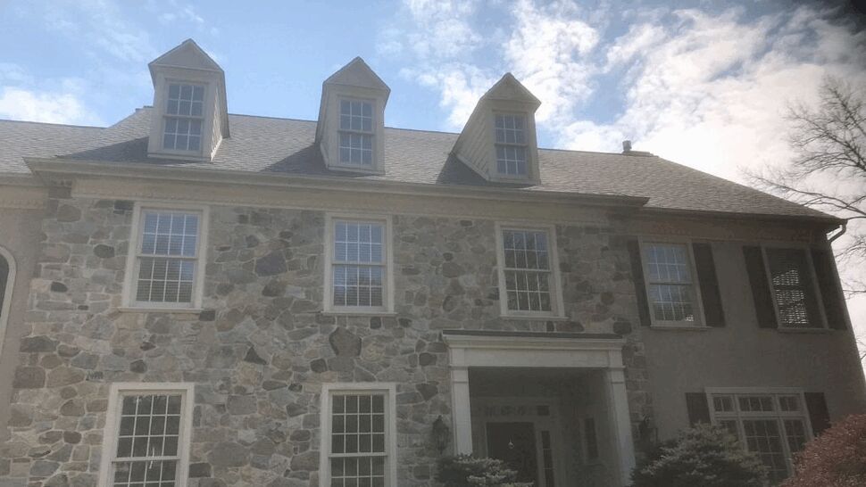 Front stone house with three dormers and asphalt roof under blue sky