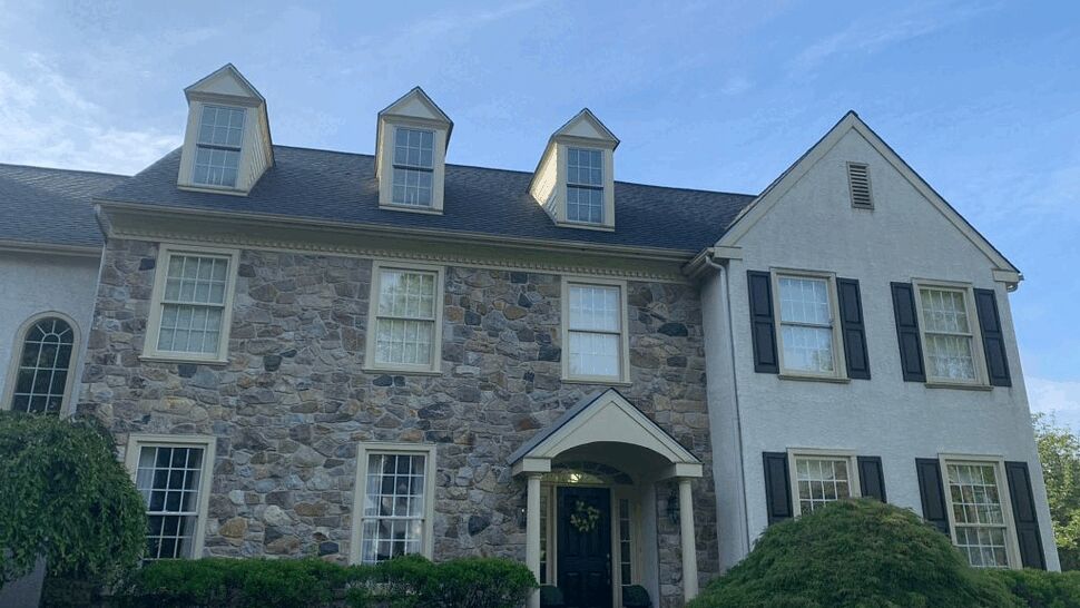 Two-story stone and stucco house with dormer windows and shingled roof.