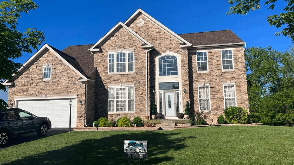 Two-Story Stone Home Exterior | Tycos Roofing And Siding Inc Stone two-story home with Tycos Roofing And Siding Inc sign on the front lawn