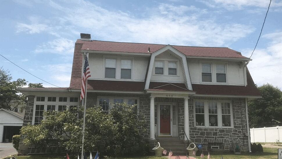 Two-story stone-front house with red shingle roof and flagpole