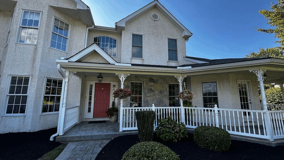 Two-story stucco house with red front door and white wraparound porch