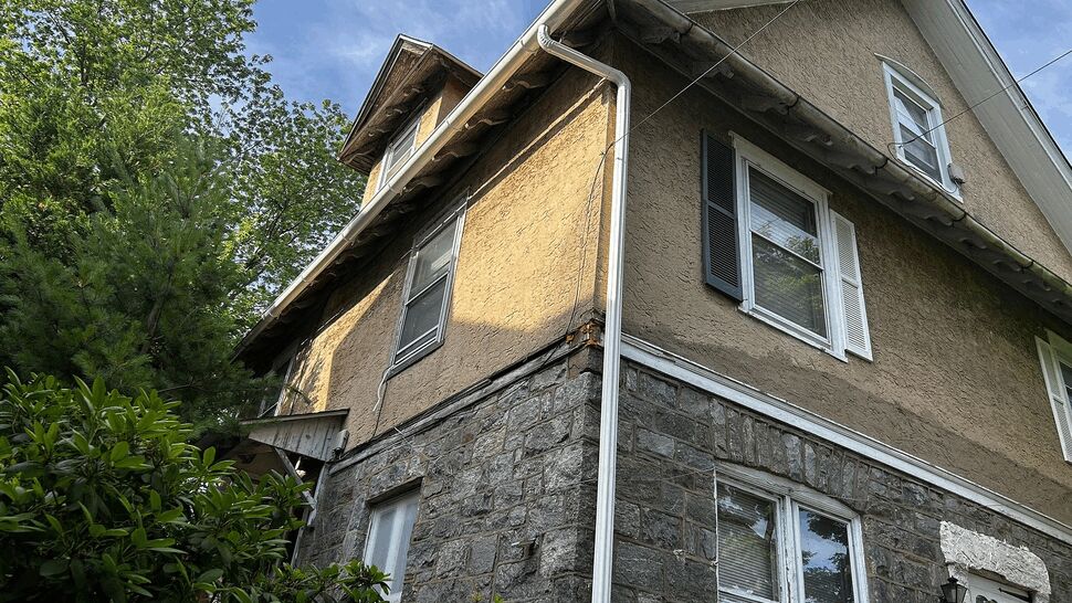 Stucco Siding and Eaves on Two-Story Home | Tycos Roofing And Siding Inc Upward view of two-story stone and stucco house showing siding, eaves, and gutters