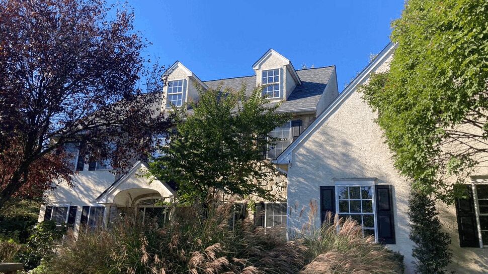 Two-story home with dormer roof, stucco siding and landscaping under clear blue sky