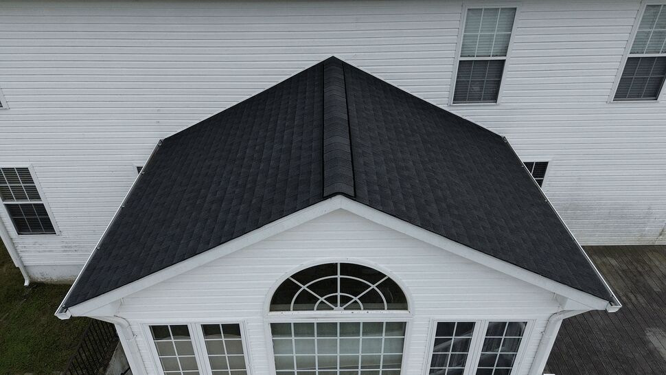 Sunroom roof and large arched window with white siding and gutters.